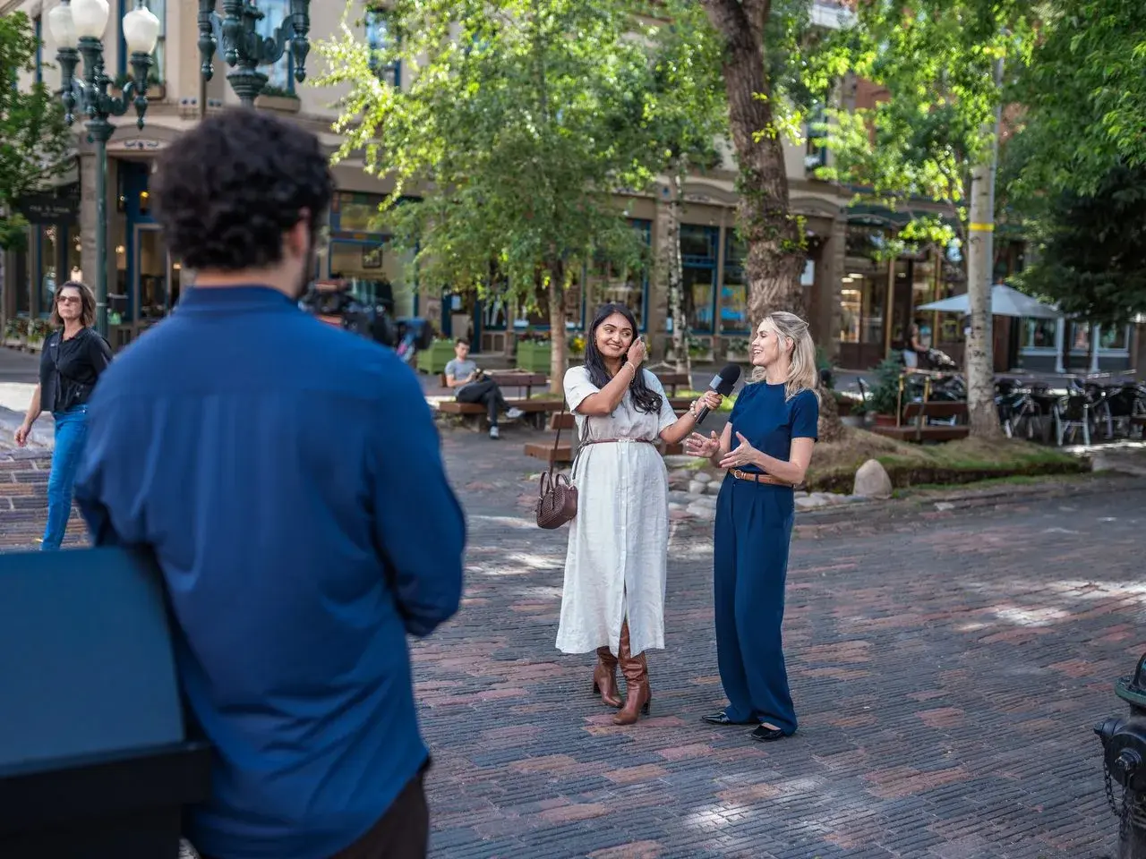 Two women smiling during an outdoor interview while an EventShark camera operator films